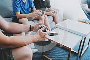 Young friends sitting on a sofa in living room and playing video games. Family relaxing time at home concept.