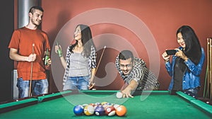 Young friends talking and playing pool at billiard table saloon