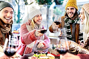 Young friends toasting red wine at restaurant patio - Happy people having fun together at winery bar wearing winter clothes -