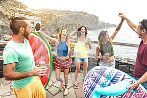 Young friends vacationer having fun at natural pool on travel location - Happy millenial people dancing and drinking cocktails