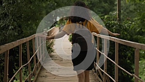 A young, frightened woman is staggering along the swaying bridge and looks down. Outside. Rear view. Real time