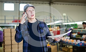 Young fruit factory foreman with papers talking on phone