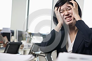 Young frustrated businesswoman sitting at desk with head in hands