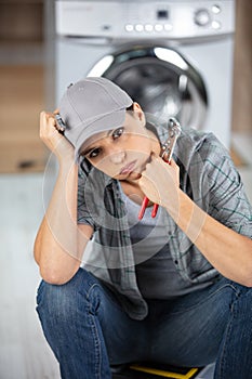 young frustrated repairwoman sitting near washing machine