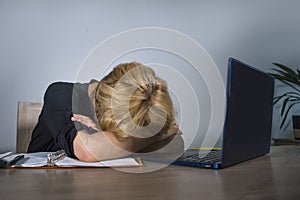 Young frustrated and stressed business woman crying sad at office desk working with laptop computer overwhelmed by paperwork workl