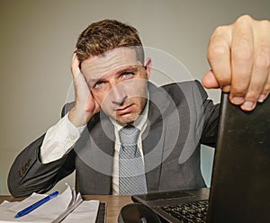 Young frustrated and stressed businessman in suit and tie working overwhelmed at office laptop computer desk suffering headache