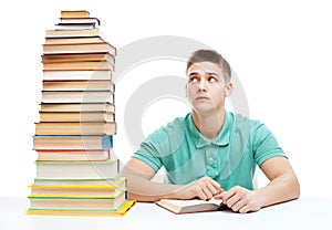 Young frustrated student sitting at the desk with high books sta