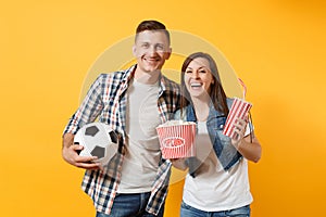 Young fun couple, woman man, football fans holding soccer ball, bucket of popcorn, plastic glass of cola, cheer up
