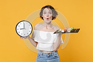 Young fun woman girl in casual clothes hold in hand clock makizushi sushi roll served on black plate traditional