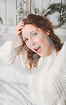 Young  fun woman with red hair in a white sweater takes a selfie in the room