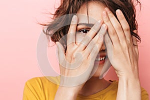 Young funny beautiful woman posing isolated over pink wall background covering face