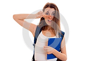 Young funny brunette student woman with blue backpack on her shoulder and folder for notebooks in hands looking at the