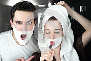 Young funny couple handsome man and beautiful singing woman both with shaving foam on their faces in bathroom playful mood