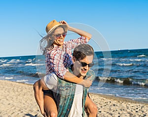 Young funny couple in sunglasses piggybacking on the beach.