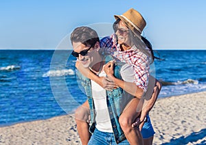 Young funny couple in sunglasses piggybacking on the beach.