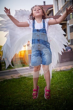 Young funny girl with wet hair after rain and white angel wings in summer day outdoors. Teenager posing on the street
