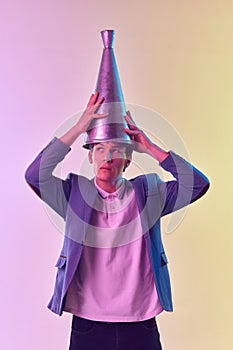 Young funny man putting retro megaphone on head, having fun isolated over light background in neon light. Concept of