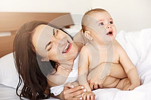 Young funny mom playing the ape her baby crying lying in bed at home.