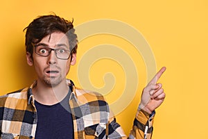 Young funny nerd guy pointing to free copy space for text on yellow studio wall