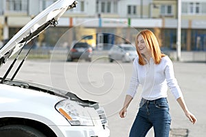 Young funny smiling woman driver near broken car with popped hood having a prbreakdown problem with her vehicle waiting for