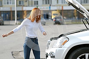 Young funny smiling woman driver near broken car with popped hood having a prbreakdown problem with her vehicle waiting for