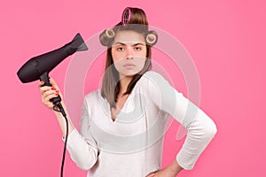 Young funny woman with hair dryer and rollers. Woman with hair dryer. Beautiful girl with straight hair drying hair with