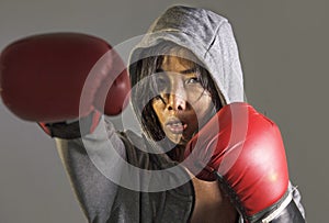 Young furious and angry Asian Chinese sporty woman in fitness top hoodie and boxing gloves training boxing workout throwing punch