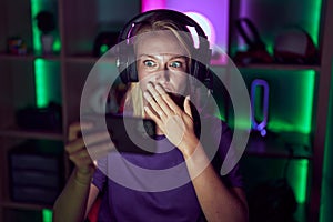 Young gamer woman playing video games with smartphone covering mouth with hand, shocked and afraid for mistake