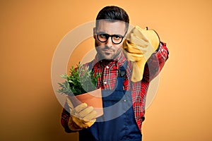 Young gardener man wearing working apron gardening plat for hobby over yellow background with angry face, negative sign showing