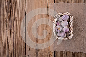 Young garlic in a basket of wicker vine lies on an old wooden rustic table. Top View