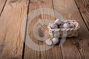 Young garlic in a small wicker basket from a vine lies on an old wooden rustic table