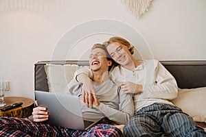 Young gay couple laughing and using laptop while resting in bed