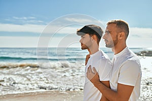 Young gay couple with serious expression looking to the horizon at the beach