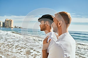 Young gay couple with serious expression looking to the horizon at the beach