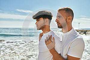 Young gay couple with serious expression looking to the horizon at the beach