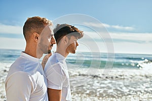 Young gay couple with serious expression looking to the horizon at the beach