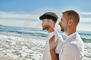 Young gay couple with serious expression looking to the horizon at the beach