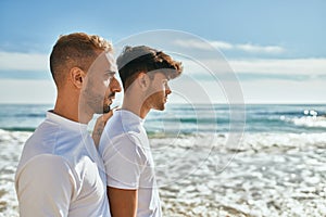 Young gay couple with serious expression looking to the horizon at the beach