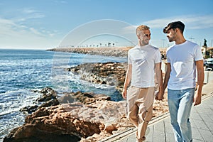 Young gay couple smiling happy walking at the beach promenade