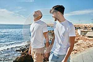 Young gay couple smiling happy walking at the beach promenade