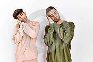 Young gay couple standing over isolated white background sleeping tired dreaming and posing with hands together while smiling with