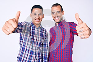 Young gay couple of two men wearing casual clothes approving doing positive gesture with hand, thumbs up smiling and happy for