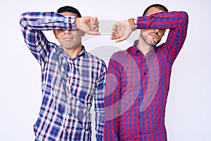 Young gay couple of two men wearing casual clothes covering eyes with arm, looking serious and sad