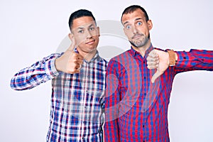 Young gay couple of two men wearing casual clothes doing thumbs up and down, disagreement and agreement expression