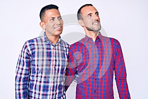 Young gay couple of two men wearing casual clothes looking away to side with smile on face, natural expression