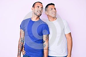 Young gay couple of two men wearing casual clothes looking away to side with smile on face, natural expression