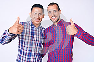 Young gay couple of two men wearing casual clothes success sign doing positive gesture with hand, thumbs up smiling and happy