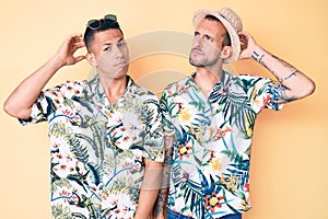 Young gay couple of two men wearing summer hat and hawaiian shirt confuse and wondering about question