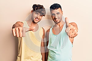 Young gay couple wearing casual clothes approving doing positive gesture with hand, thumbs up smiling and happy for success