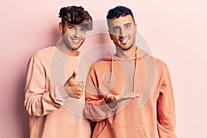 Young gay couple wearing casual clothes showing palm hand and doing ok gesture with thumbs up, smiling happy and cheerful